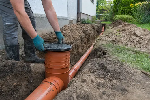 Pracovník osazuje revizní šachtu na nové kanalizační potrubí ve výkopu u domu
