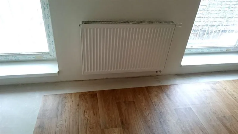 Nový bílý deskový radiátor napojený na rozvody topení